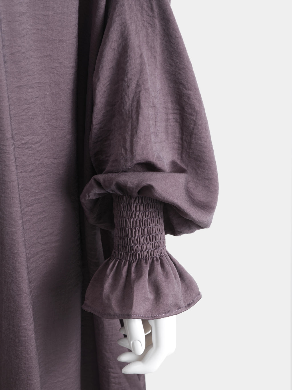 Close-up of a dark purple jilbab with smocked cuffs on a mannequin against a white background