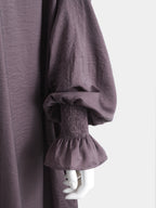 Close-up of a dark purple jilbab with smocked cuffs on a mannequin against a white background