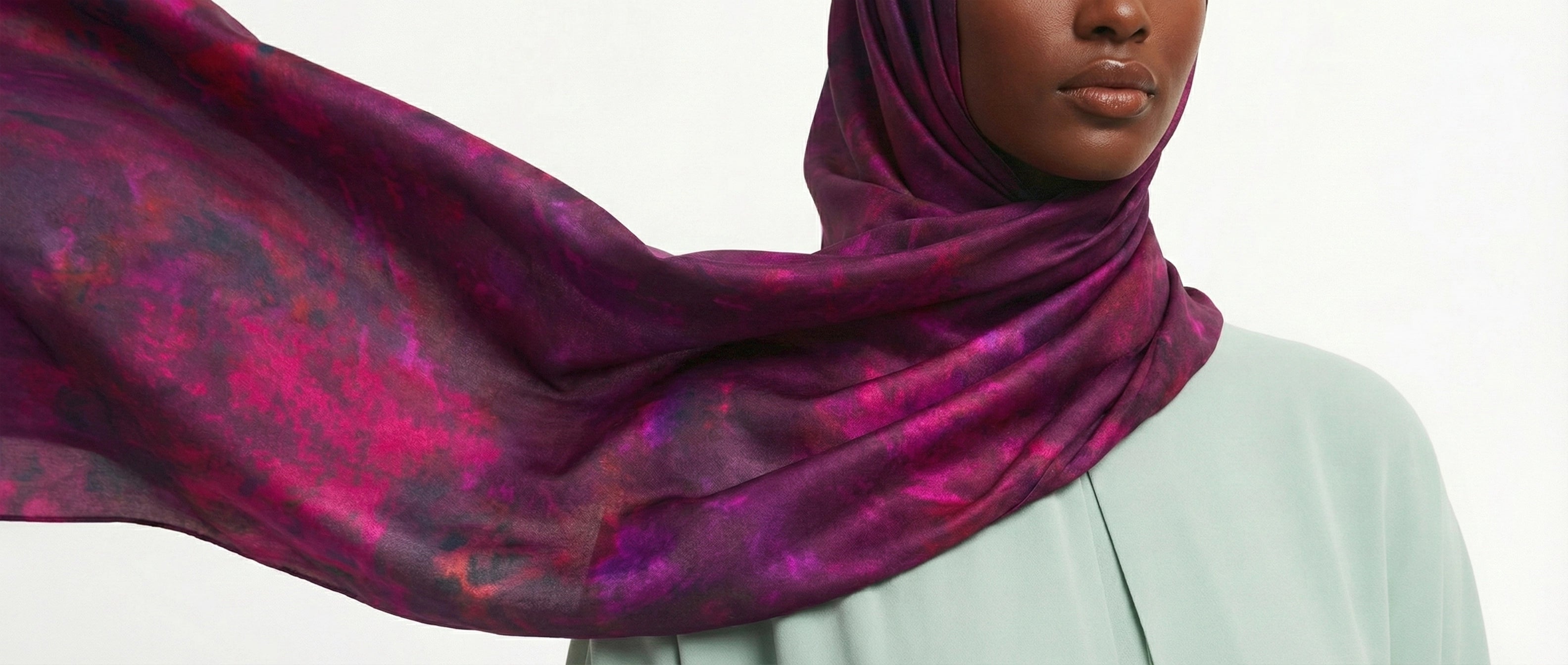 Person wearing a vibrant purple hijab with pink patterns on a plain background